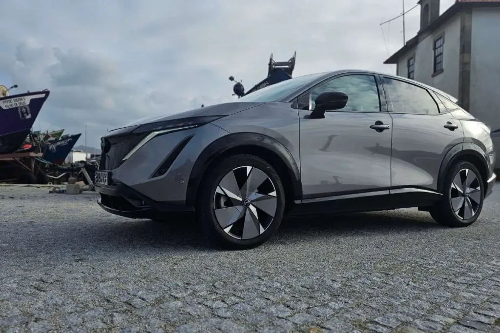 Nissan Ariya: um bom SUV com um senão 3 Nissan Ariya visto de lado, estacionado em frente a barcos de pesca artesanal.